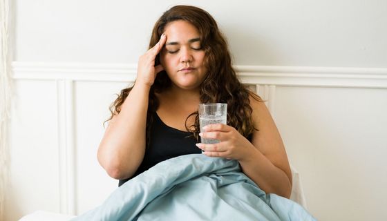 Junge Frau, sitzt mit Kopfschmerzen im Bett.