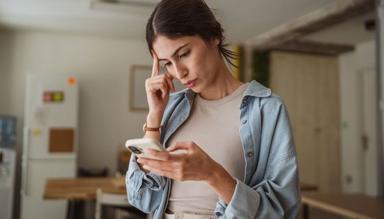 Frau fasst sich kritisch an den Kopf, während sie etwas auf ihrem Smartphone liest.