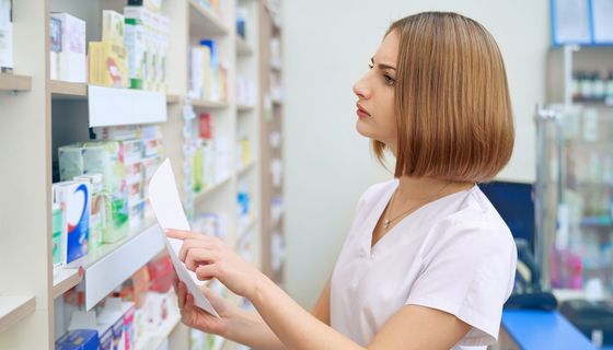 Apothekerin sucht nach einem Medikament im Regal.