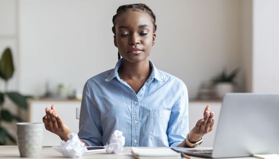 Eine Jugendliche sitzt am Schreibtisch, zwei zerknüllte Blätter Papier vor ihr, und entspannt sich mittels Yoga-Atemtechnik.