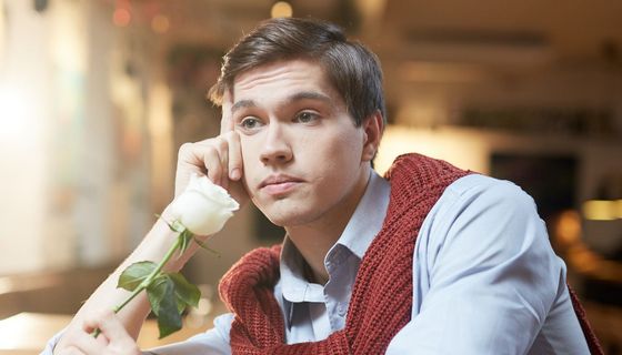 Junger Mann wartet zweifelnd auf sein Date – wohl schon länger. In einer Hand hält er eine Rose.