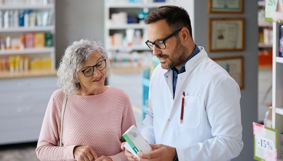 Ein Apotheker berät eine ältere Kundin zu einem Medikament.