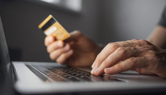 Online Bezahlung: Männerhände halten eine Kreditkarte und bedienen das Maus-Pad eines Laptops.
