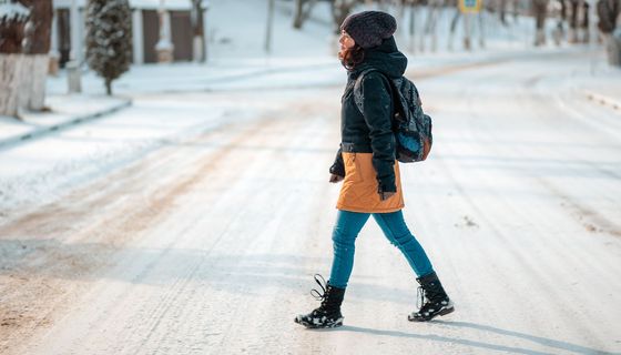 Frau in warmer Winterkleidung geht über eine vereiste Straße.
