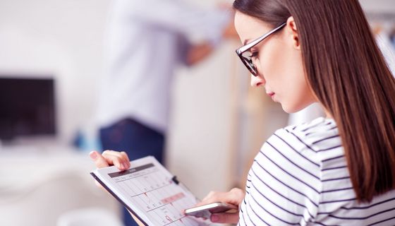 Frau blickt auf einen Monatskalender, in dem einzelne Tage rot markiert sind – darunter auch eine Strecke von vier Tagen hintereinander.