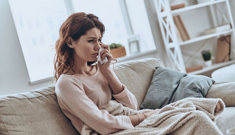 Eine junge Frau sitzt auf dem Sofa und weint.
