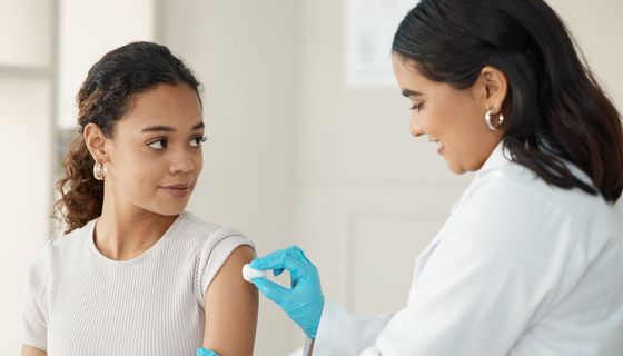 Eine Ärztin definiziert die Haut am Oberarm einer jungen Frau, um sie auf eine Impfung vorzubereiten.