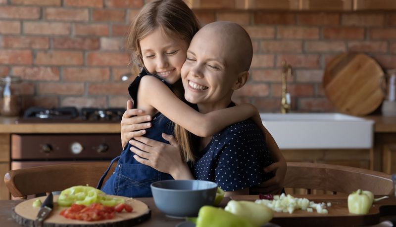 Krebspatientin umarmt ein Mädchen, vor ihnen liegt geschnittenes Gemüse.