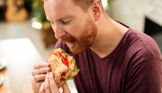 Ein Mann beißt in ein Sandwich mit Tomate, Salat und Schinken.