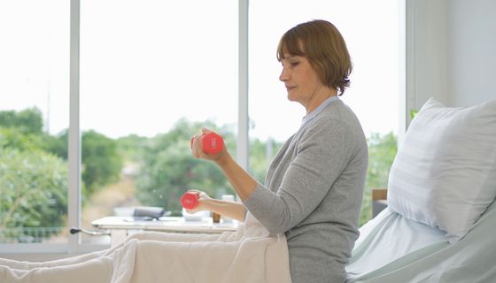 Patientin macht im Krankenbett Übungen mit Hanteln.