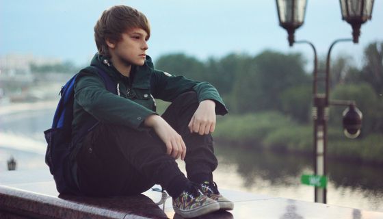 Ein Junge, etwa 11 bis 14 Jahre alt, sitzt alleine und schaut nachdenklich.