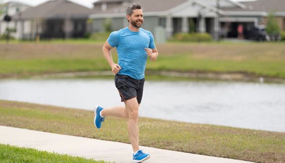 Mann mit Vollbart und graumelierten Haaren joggt an einem Kanal entlang.