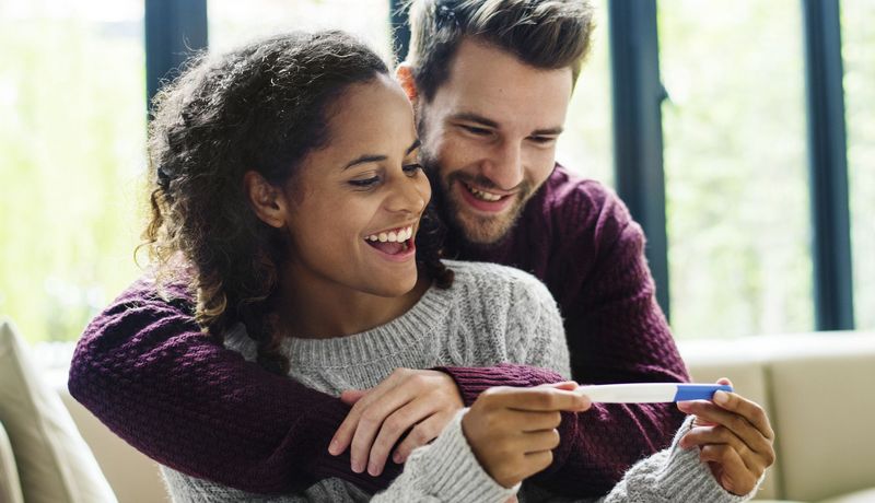 Ein Paar freut sich, die Frau hält einen Schwangerschaftstest in den Händen.