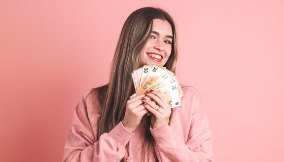 Eine junge Frau hält fröhlich ein Bündel 50-Euro-Scheine