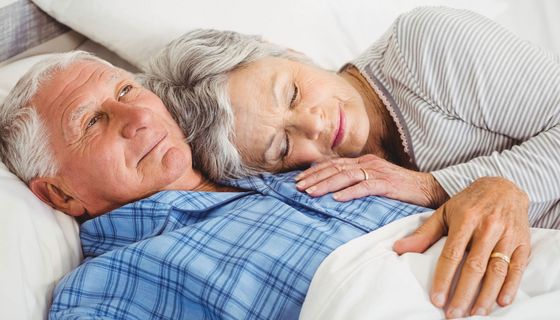 Ein Paar jenseits des 60. Lebensjahrs kuschelt im Bett.