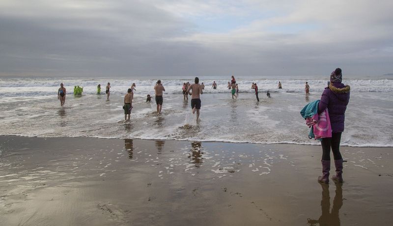 Menschen laufen am winterlichen Strand ins Wasser.