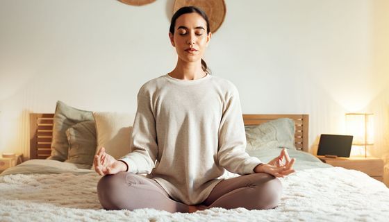Frau meditiert auf dem Bett.