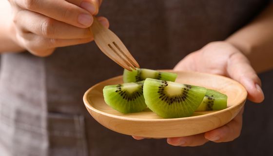 Jemand hält eine Schale mit aufgeschnittene Kiwi in einer Hand und piekst eine Scheibe auf.