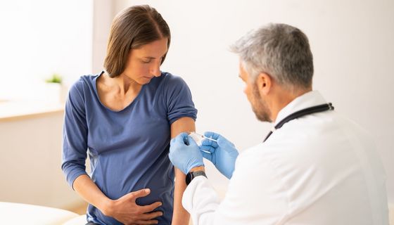 Ein Arzt impft vorsichtig eine Schwangere.
