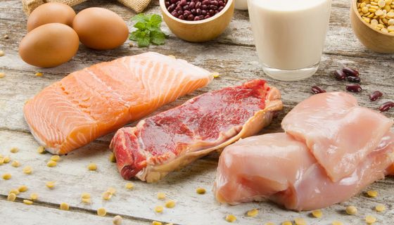 Auf einer Holzunterlage liegen drei Eier, ein Stück Lachs, Rindfleisch und Hühnerfleisch.