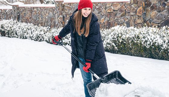 Eine junge Frau schippt gutgelaunt Schnee.