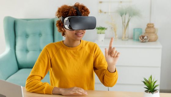 Eine junge Frau sitzt mit einer VR-Brille an einem Schreibtisch.